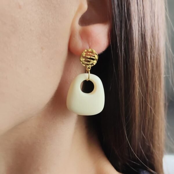 Boucle d'oreille pendante avec pendentif en forme de trapèze en résine écru et clou d'oreille en acier inoxydable martelé doré.