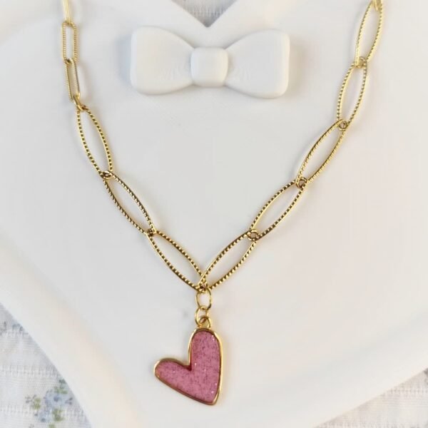 Collier doré avec pendentif cœur rose pailleté posé à plat