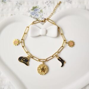 Bracelet avec breloques en acier inoxydable doré et résine noire et orange. Le bracelet est posé sur un plateau blanc.